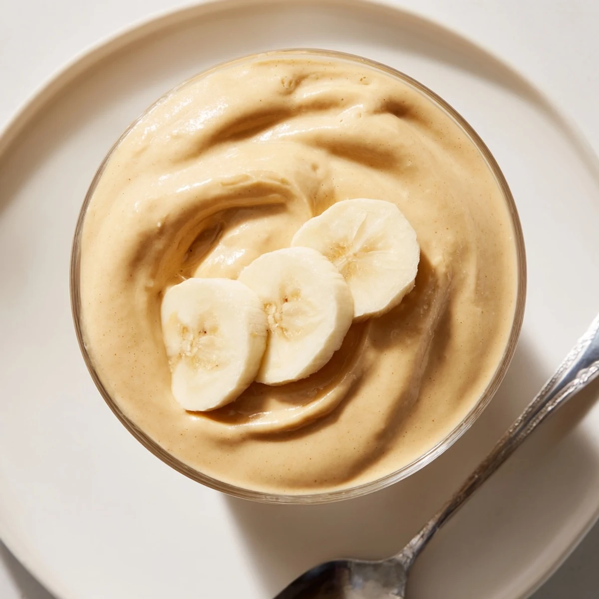 A tall glass of Peanut Butter Banana Smoothie, swirled with creamy texture and topped with whipped cream.