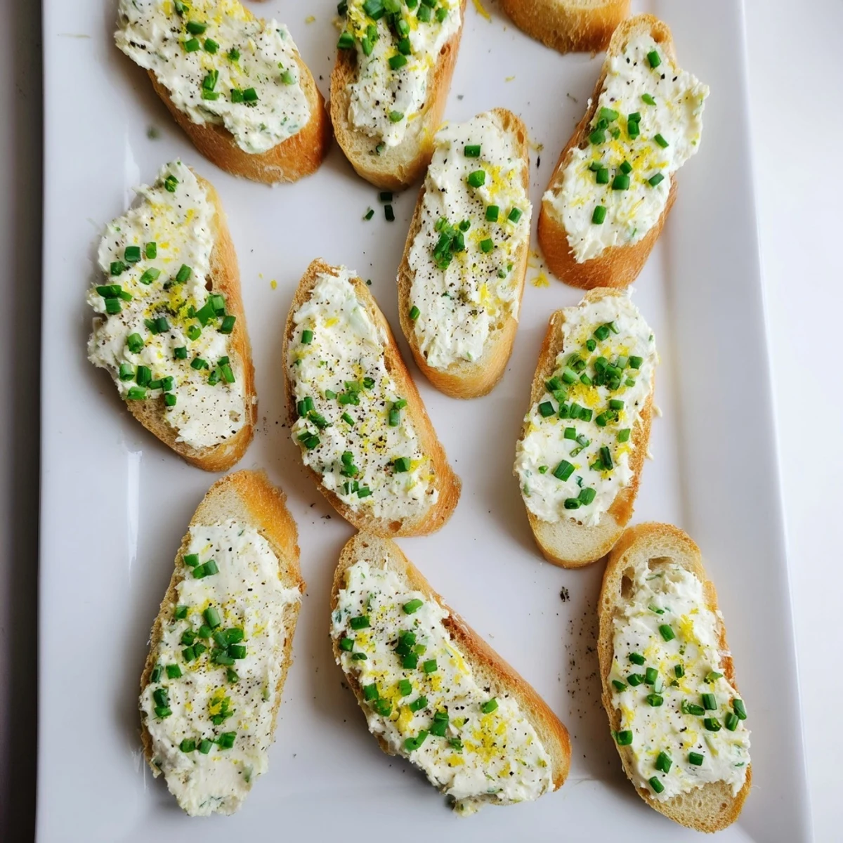 Golden, crisp vodka butter crostini arranged on a rustic slate platter, topped with fresh chives and lemon zest for an elegant appetizer.