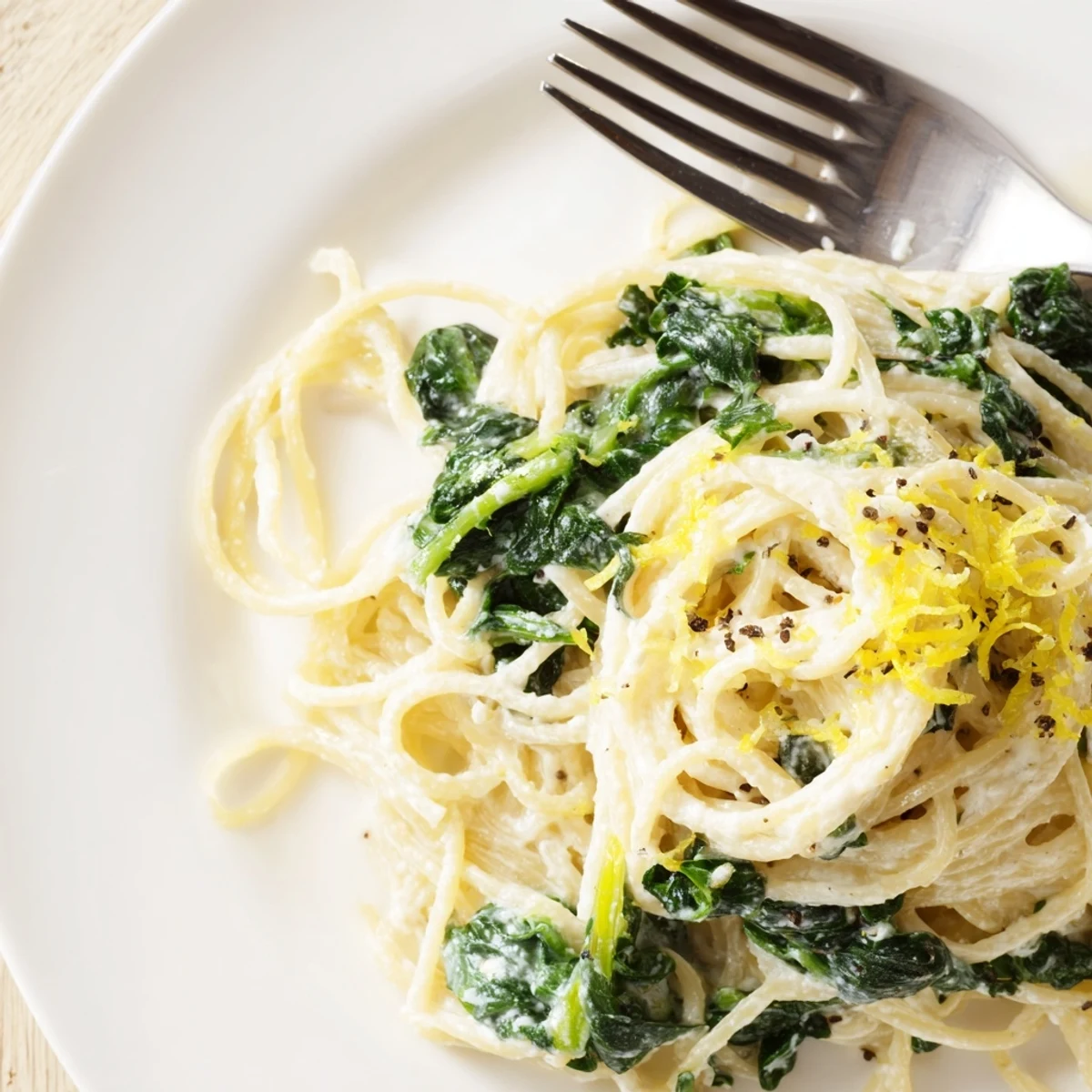 Freshly cooked spaghetti tossed in a creamy lemon sauce with wilted spinach, served on a white plate.
