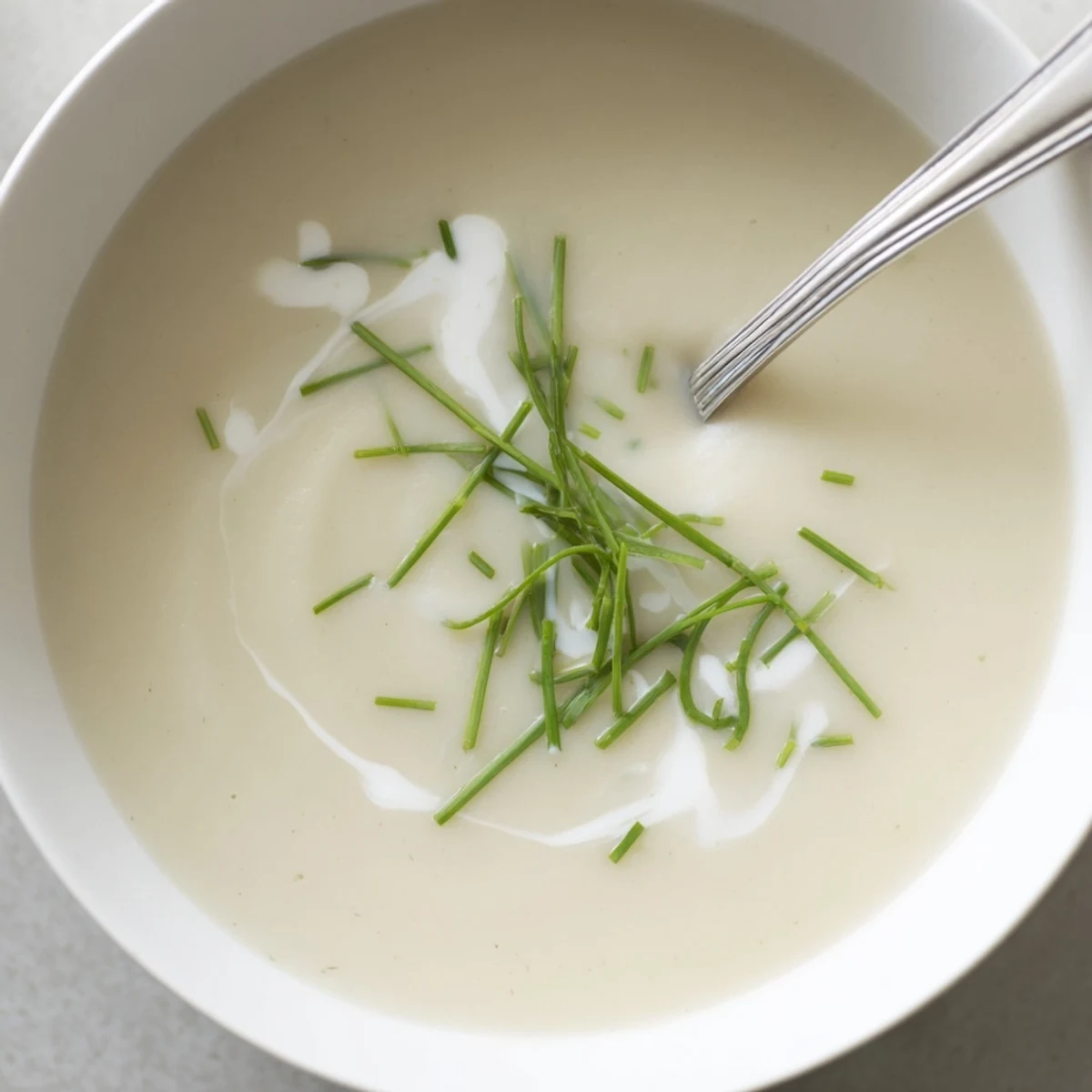 Silky celery root bisque poured into a white bowl, garnished with fresh chives and a swirl of cream.  