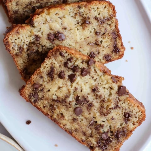 A slice of warm chocolate chip banana bread, showcasing melty chocolate and a golden crust.