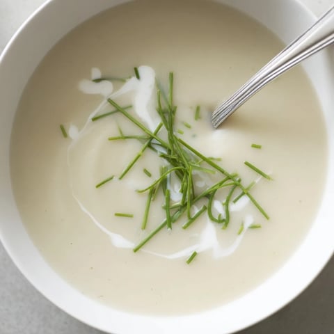 Silky celery root bisque poured into a white bowl, garnished with fresh chives and a swirl of cream.  