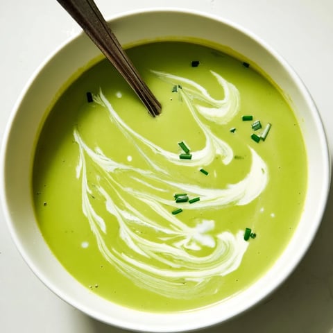A steaming bowl of creamy broccoli soup garnished with a swirl of cream and fresh chives on a rustic table.  
