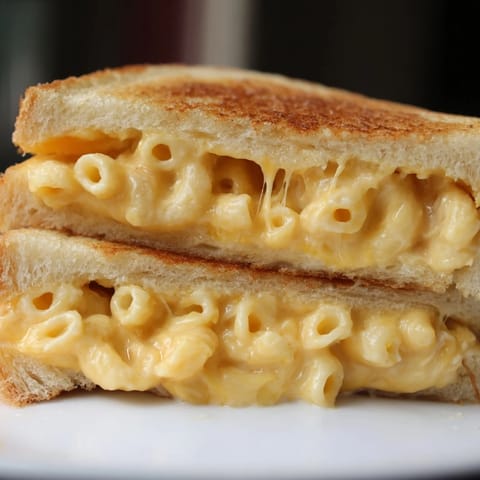 Two halves of a Mac & Cheese Grilled Cheese sandwich stacked on a cutting board, showing the creamy macaroni and cheddar inside.  