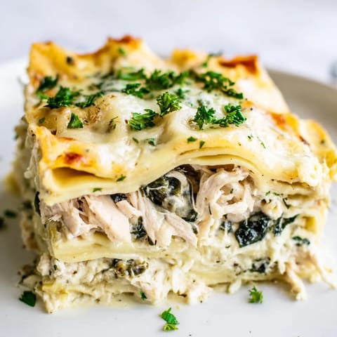 A close-up of a freshly baked Chicken Alfredo Lasagna slice, steam rising from melted mozzarella and tender chicken.  