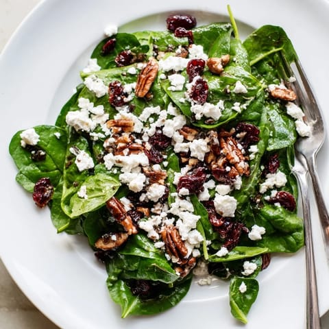 A finished Spinach Goat Cheese Salad tossed in tangy balsamic vinaigrette, garnished with candied pecans and ready for a light lunch.