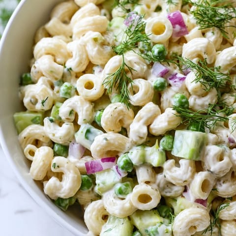 Creamy dill pickle pasta salad served chilled in a white bowl, garnished with fresh dill, ready for a summer picnic or potluck.  