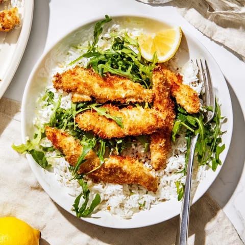 Crispy Parmesan chicken cutlets sliced over rice and greens, drizzled with lemon for a bright finish.