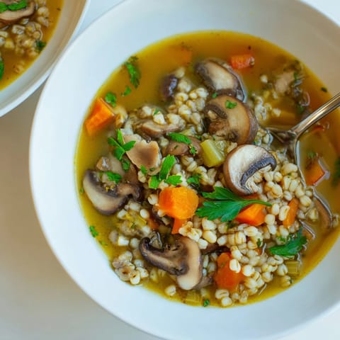 Close-up of a ladle scooping hearty Mushroom and Barley Soup from a pot, revealing carrots and celery in a rich, herb-infused broth.